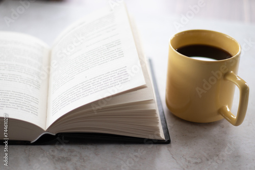 Open book with black cover and yellow cup of coffee on the table. Close up view.