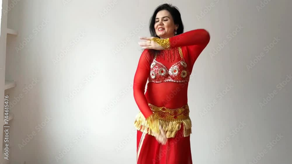 A dancer in a red suit is dancing an oriental dance on a white background. A professional dancer dances oriental belly dance. Sexy woman in red dress dances a seductive dance in a white studio A dancer in a red suit is dancing an oriental dance on a white background. A professional dancer dances oriental belly dance. Sexy woman in red dress dances a seductive dance in a white studio