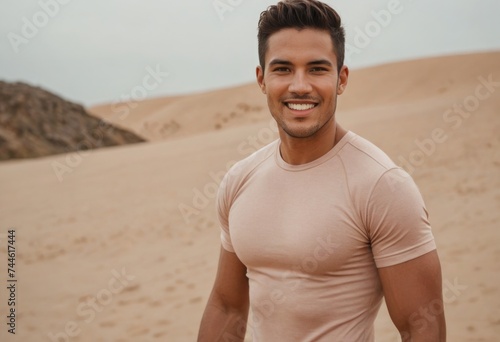 A fit man in a desert setting, wearing a light peach shirt that complements the sandy background.