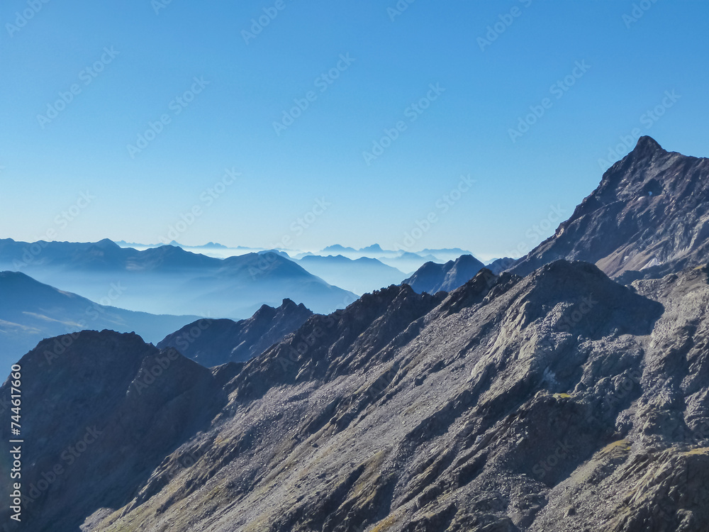 Panoramic view from majestic mountain peak of Hochschober, Schober Group, High Tauern National Park, East Tyrol, Austria. Wanderlust Austrian Alps in summer. Misty rugged ridges against clear blue sky Panoramic view from majestic mountain peak of Hochschober, Schober Group, High Tauern National Park, East Tyrol, Austria. Wanderlust Austrian Alps in summer. Misty rugged ridges against clear blue sky