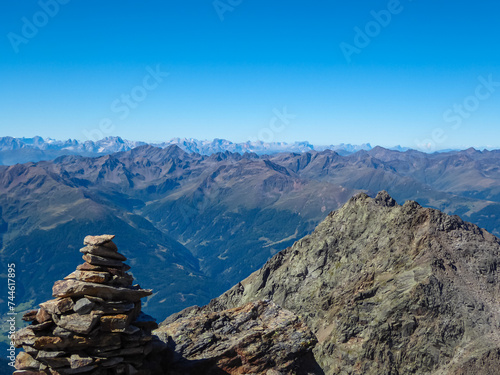 Cairns of rock with panoramic view from majestic mountain peak of Hochschober, Schober Group, High Tauern, East Tyrol, Austria. Wanderlust Austrian Alps in summer. Misty rugged ridges against blue sky © Chris