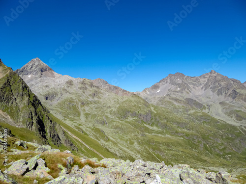 Hiking trail on alpine terrain surrounded by majestic mountain peaks Schober Group, High Tauern, East Tyrol, Austria. Austrian Alps in summer. Rugged ridges against blue sky. Looking at mount Glödis photo