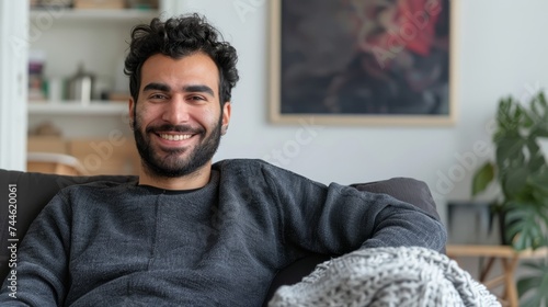In this concept, a happy Middle Eastern guy enjoys a weekend break or weekend free time on a comfortable sofa in his living room. An image of a happy casual man enjoying weekend free time or a break