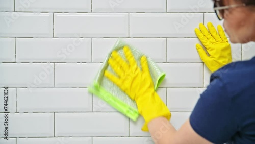Close-up woman in gloves cleaning tiles in shower in bathroom