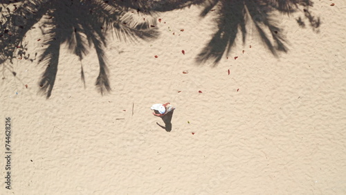 Sand beach palm trees background aerial top down view. Woman in white dress walking empty perfect coastline, ideal shore, relax, enjoy outdoor lifestyle travel on summer holiday vacation. Drone shot.