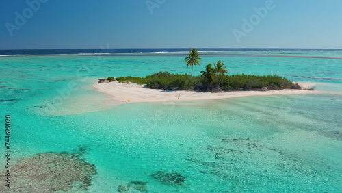 Travel concept background - small tropical island in turquoise water coral reef sea. Perfect sand beach, palm tree, crystal water. Travel written on sand, woman waving hands. Aerial drone flight