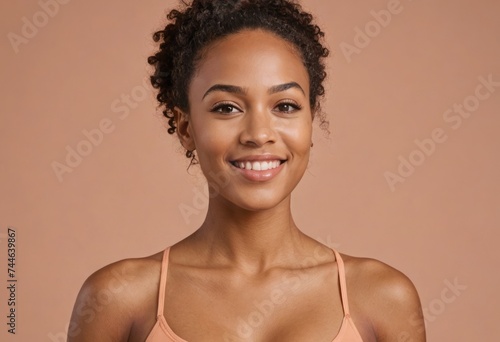 A young woman with a sleek hairstyle in a spaghetti strap top. Her poised look against the warm background creates an image of effortless grace.