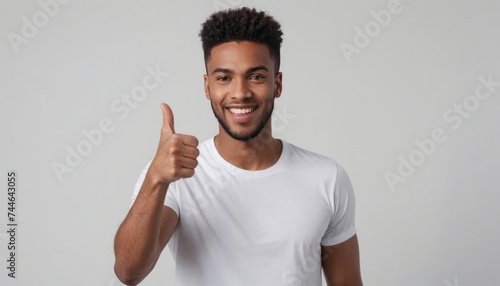 A young black man in a white t-shirt shows a thumbs up with a radiant smile and relaxed demeanor.