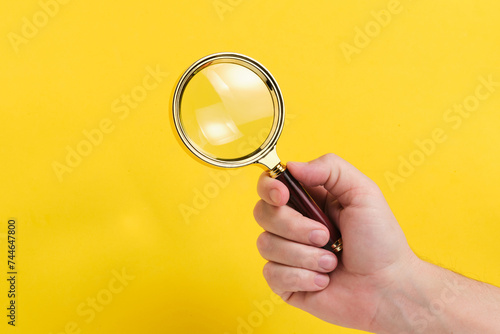 Magnifying glass in hand yellow background.