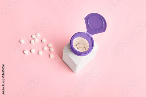 Jar with pills and scattered pills on pink background