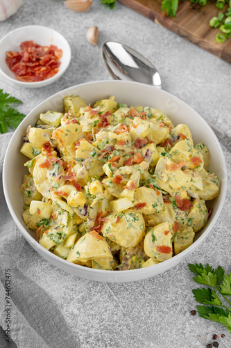 Salad of potatoes, eggs, bacon and fresh herbs with mayonnaise and yogurt dressing in a bowl on a gray concrete background.