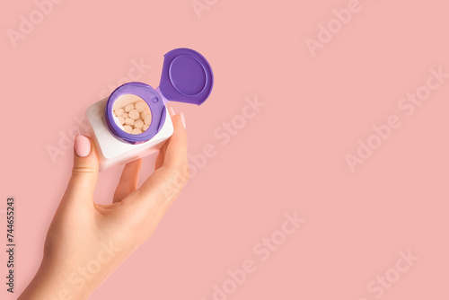 Fototapeta Naklejka Na Ścianę i Meble -  Female hand holding an open jar of pills on a pink background