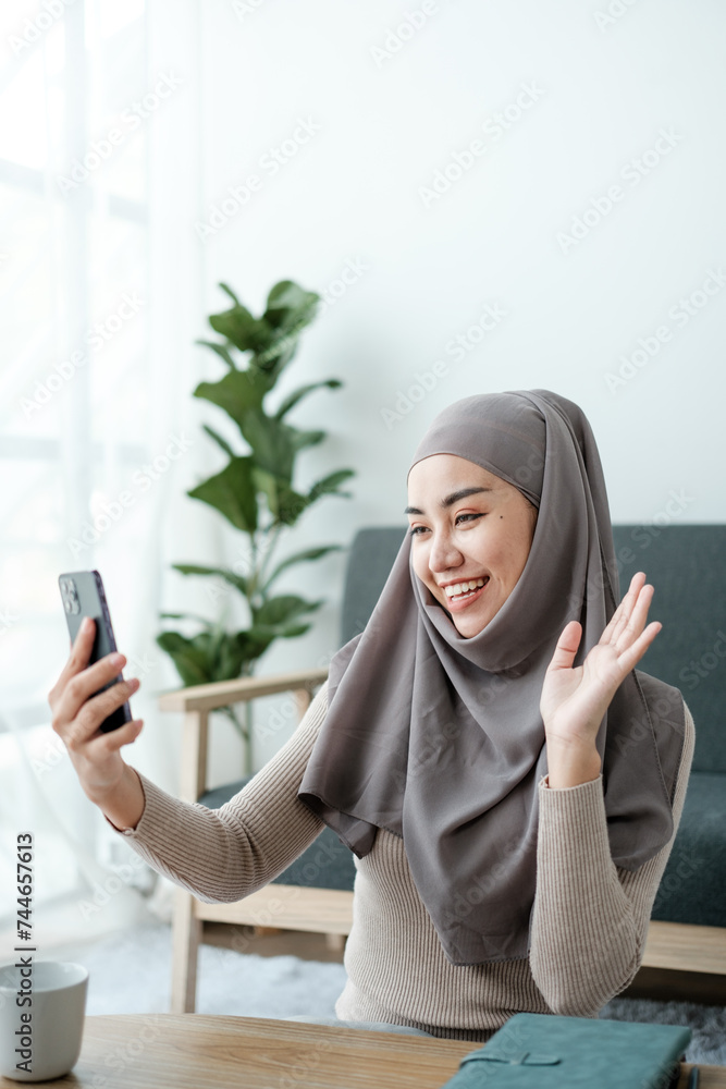 A Beautiful asian woman in hijab talks on video call, online meeting with colleagues and clients, woman cheerfully waves her hand and greets interlocutors online. A Beautiful asian woman in hijab talks on video call, online meeting with colleagues and clients, woman cheerfully waves her hand and greets interlocutors online.