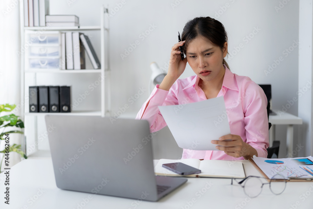 Young Asian woman puts her hands on her head feeling tired, irritated and stressed from hard work at the office and dissatisfied with her job while looking at report documents. Young Asian woman puts her hands on her head feeling tired, irritated and stressed from hard work at the office and dissatisfied with her job while looking at report documents.