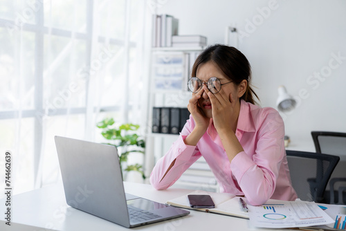 Young Asian woman puts her hands on her head feeling tired, irritated and stressed from hard work at the office and dissatisfied with her job while looking at report documents.