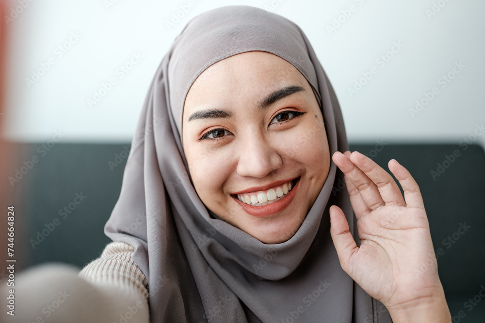 A Beautiful asian woman in hijab talks on video call, online meeting with colleagues and clients, woman cheerfully waves her hand and greets interlocutors online. A Beautiful asian woman in hijab talks on video call, online meeting with colleagues and clients, woman cheerfully waves her hand and greets interlocutors online.