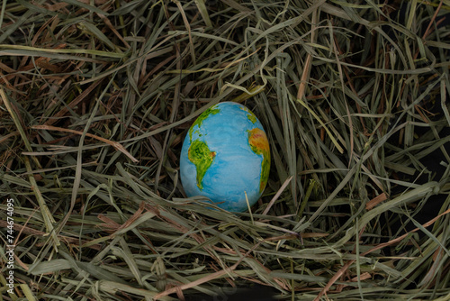 Easter egg hand painted to resemble the Planet Earth, nestled in green grass