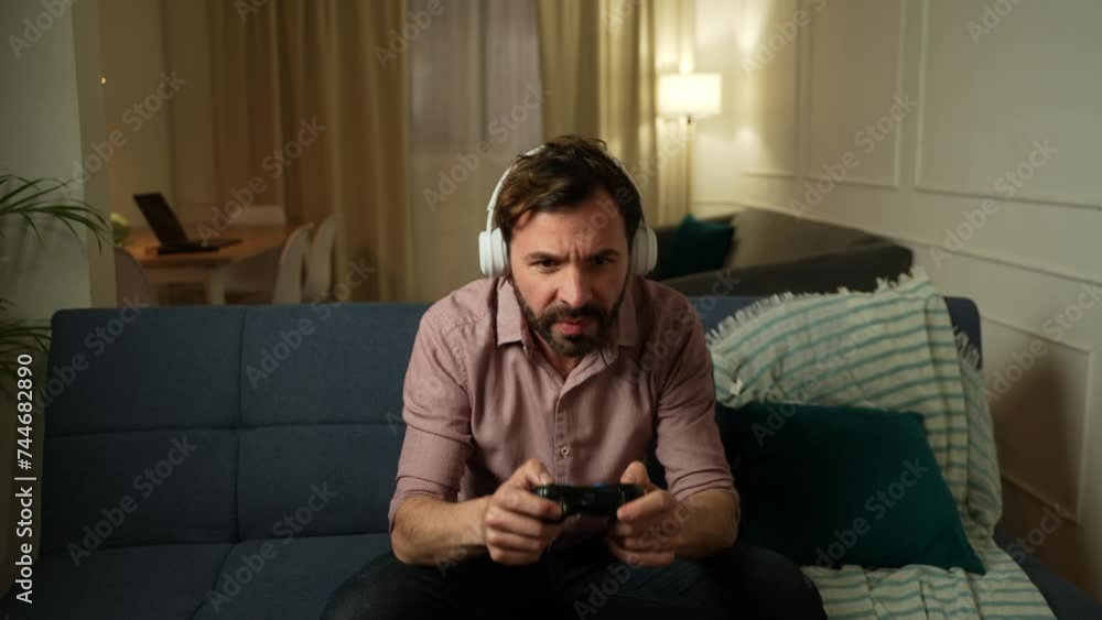 Man on his 30s wearing headphones and playing videogames at home at night Man on his 30s wearing headphones and playing videogames at home at night