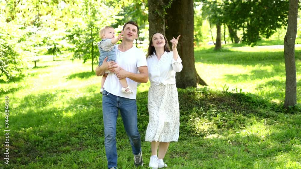 Parents go to the park, dad holds the child in his arms, looking at everything around him. Have a nice family walk in nature. Family vacation concept, happy family moments, parenthood Parents go to the park, dad holds the child in his arms, looking at everything around him. Have a nice family walk in nature. Family vacation concept, happy family moments, parenthood