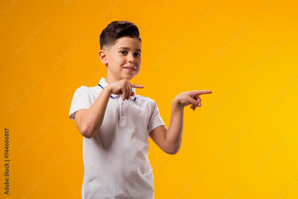 Smiling child boy pointing to an empty place on yellow background. Advertisement concept Smiling child boy pointing to an empty place on yellow background. Advertisement concept
