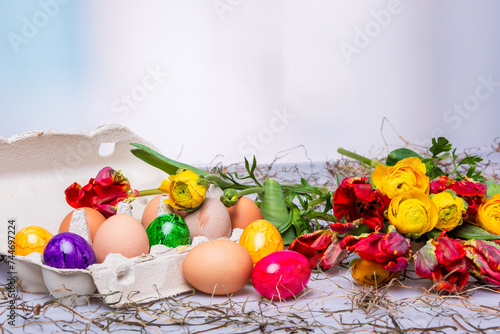 Bunte Ostereier auf einem Tisch mit Bumenstrauß als Postkartenmotiv zu Ostern