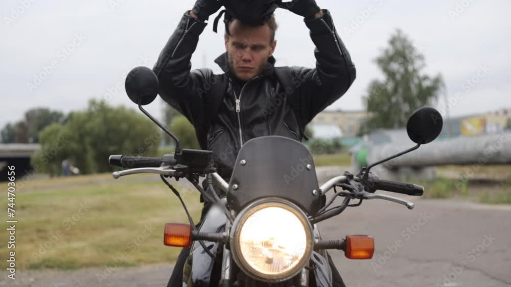 male motorcyclist in a helmet and leather jacket and gloves on a classic motorcycle in the city takes off his helmet. male motorcyclist in a helmet and leather jacket and gloves on a classic motorcycle in the city takes off his helmet.