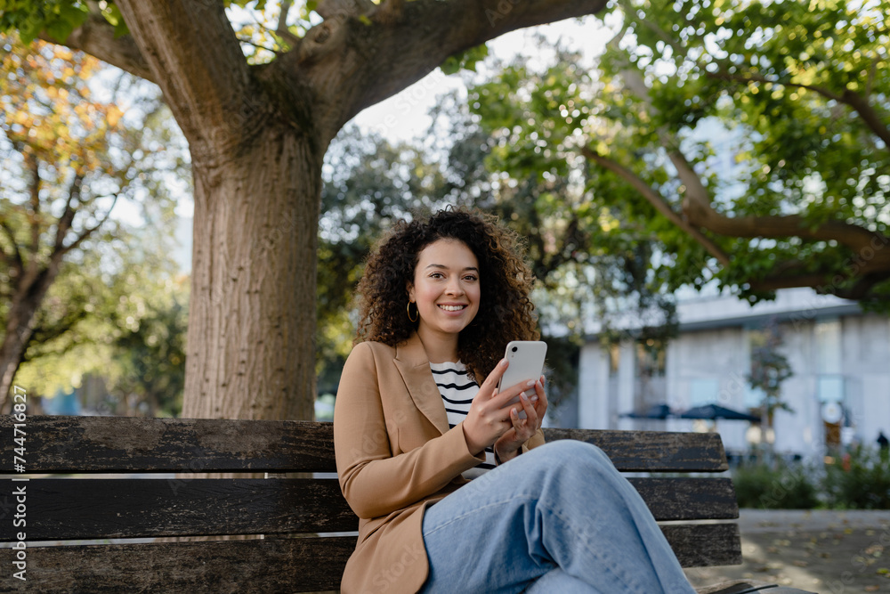 pretty curly smiling woman walking in city street in stylish jacket, using smartphone pretty curly smiling woman walking in city street in stylish jacket, using smartphone