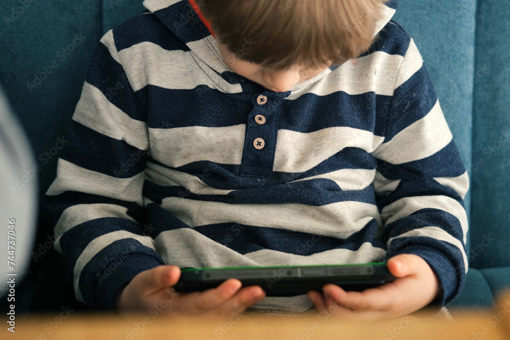 One toddler boy using smartphone sitting in cafe, restaurant. Child looking at mobile phone, modern parenting concept. Lifestyle with digital gadget devices. Bored kid relax with play game on a cell. One toddler boy using smartphone sitting in cafe, restaurant. Child looking at mobile phone, modern parenting concept. Lifestyle with digital gadget devices. Bored kid relax with play game on a cell.