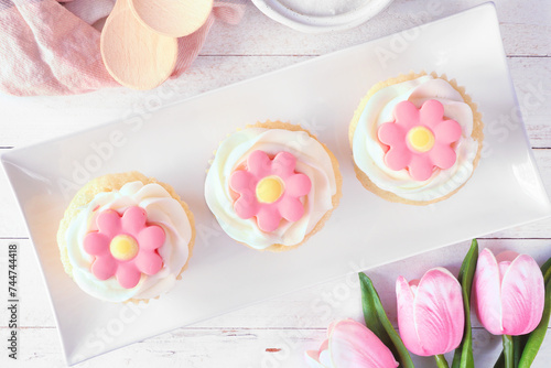 Plate of pink spring flower cupcakes. Above view table scene with a white wood background.