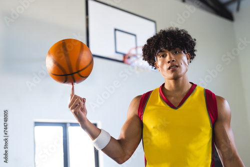 Young biracial man spins a basketball on his finger in a gym photo