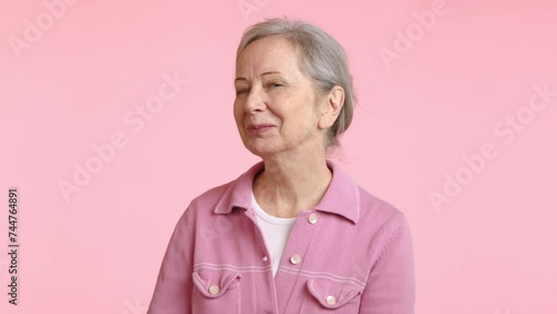 A happy senior woman in a pink jacket is smiling warmly, her eyes twinkling with joy and reflecting a heart full of contentment and pleasure.  photo