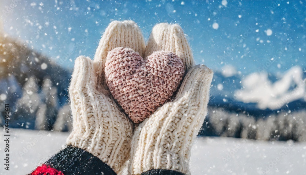 female hands in knitted mittens with snowy heart against snow background