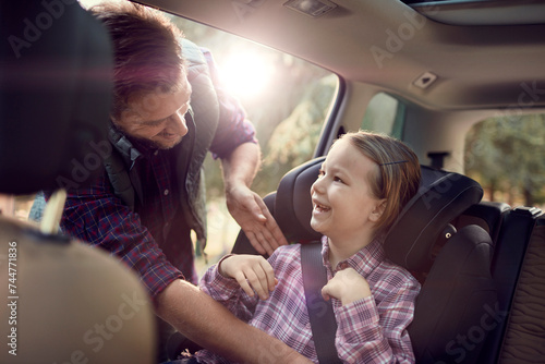 Father putting seatbelt on daughter in car backseat photo