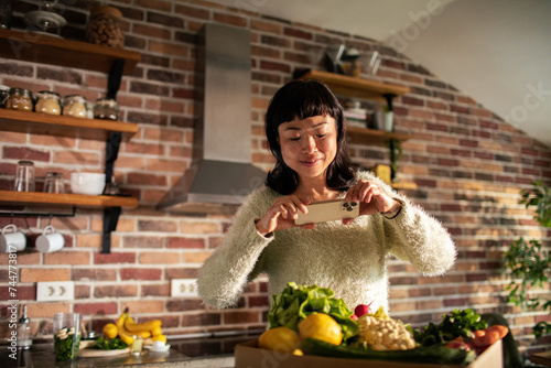 Woman taking photo of fresh vegetables with smartphone in kitchen © Vorda Berge