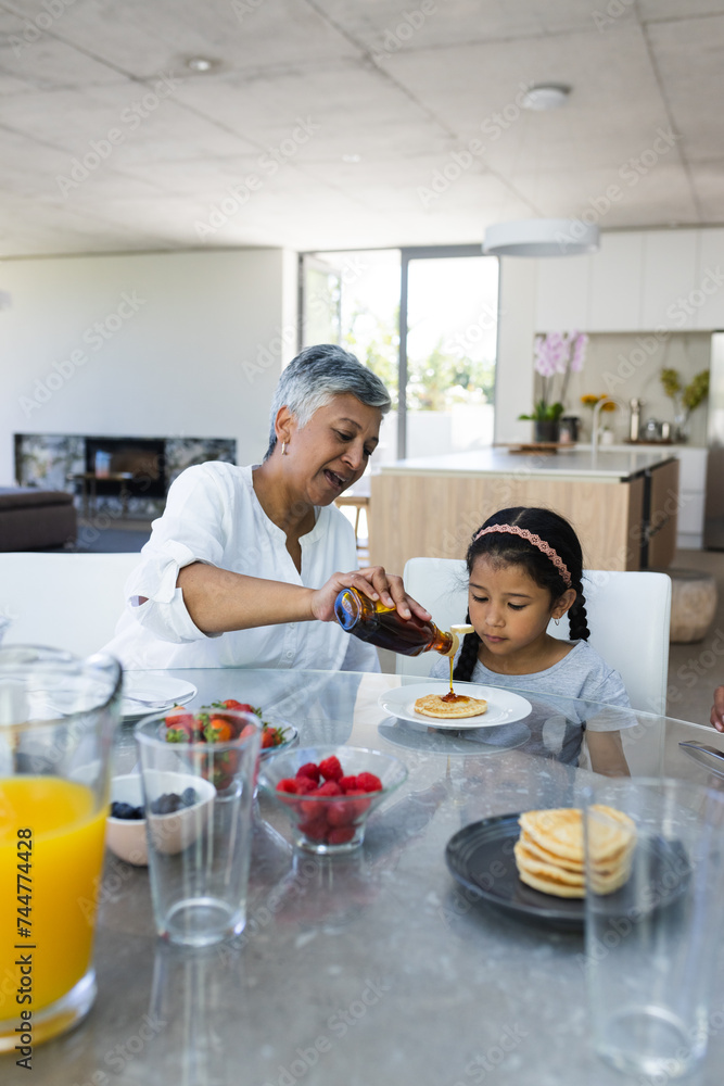 Biracial grandmother serves breakfast of pancakes to a biracial granddaughter at home Biracial grandmother serves breakfast of pancakes to a biracial granddaughter at home