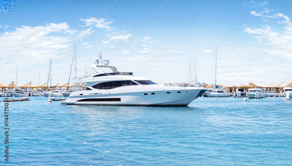 A sleek and stylish white motor yacht is docked at a marina, surrounded by other luxury yachts and sailboats and blue sky 