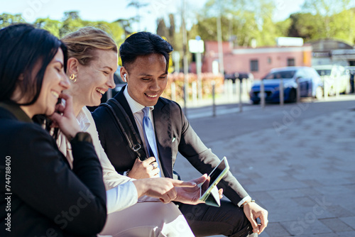 Three corporate professionals enjoy a light moment while reviewing data on a tablet outdoors