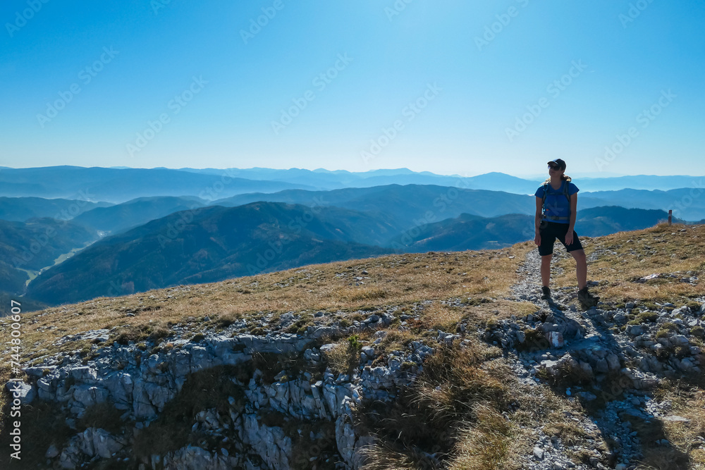Hiker woman on golden alpine meadow on the way to mount Hohe Veitsch in Mürzsteg Alps, Styria, Austria. Panoramic view of mountain ridges in remote Austrian Alps. Wanderlust in autumn. Tranquil serene