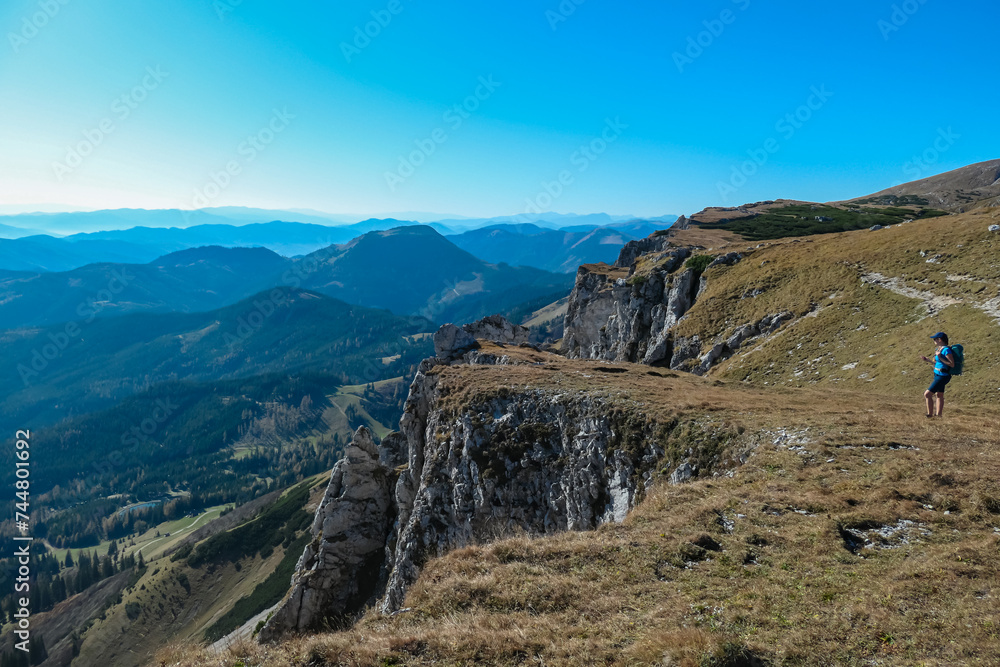 Hiker Woman on edge of steep cliff on top of mountain peak Hohe Veitsch, Mürzsteg Alps, Styria, Austria. Idyllic hiking trail alpine terrain. Wanderlust remote Austrian Alps in autumn. Rock formation