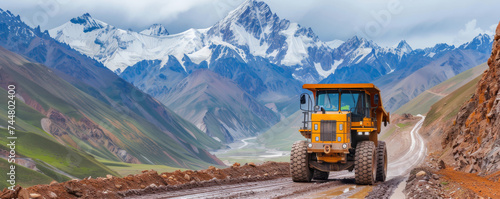 Heavy machine rumbles defiantly along road against mountains. Heavy dump truck presses onward with tires carving path through rocky terrain. photo