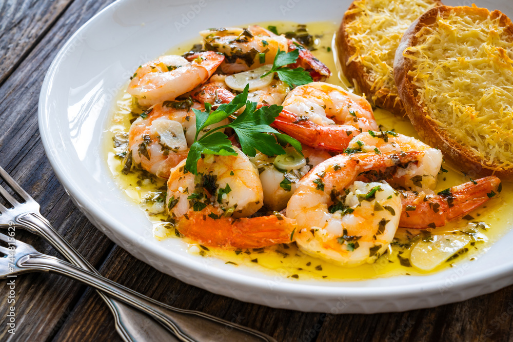 Fried shrimps with garlic and parsley in olive oil and toasted bread with parmesan cheese on wooden table