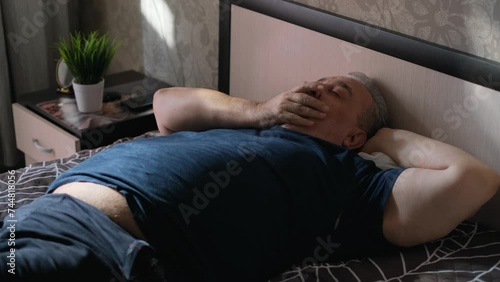 Sleepy overweight man yawning while lying on bed photo