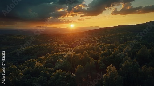 A bird's-eye view reveals a breathtaking sunset casting its warm, dramatic colors over forested hills, creating a scene of serene beauty and natural splendor.