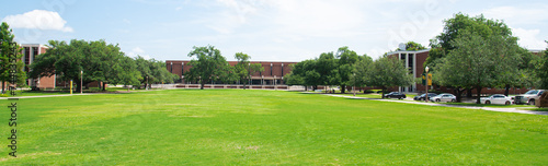 Panorama grassy campus quad courtyard, several historic buildings in background, large meadow front yard college green space under sunny summer cloud blue sky in Texas, education, landscaping photo