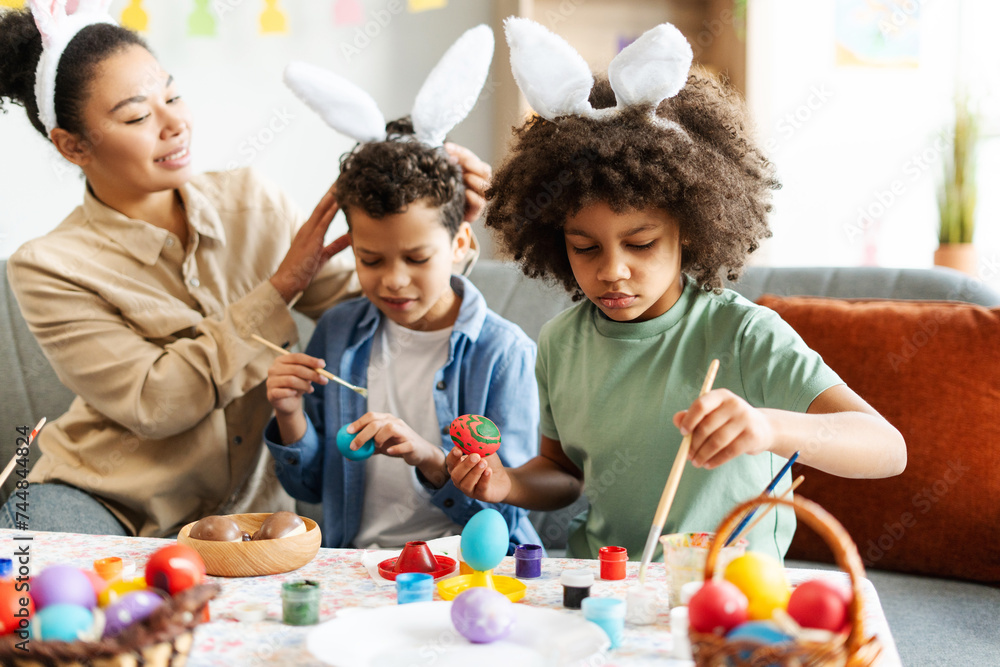 Happy christian African American family wearing cute bunny ears painting Easter eggs at home