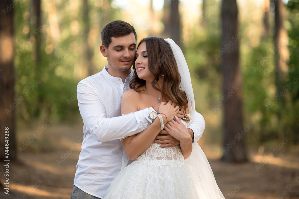 The young groom and bride, in the forest, lovingly embrace The young groom and bride, in the forest, lovingly embrace
