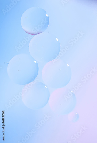 Macro drops of oil on the surface of the water. Delicate cosmetic bubbles background for advertising cosmetic products in soft blue tones, gradient. Vertical photo.