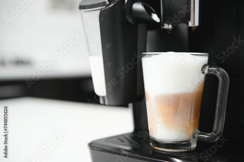 Modern coffee machine with glass cup of latte on white marble countertop in kitchen