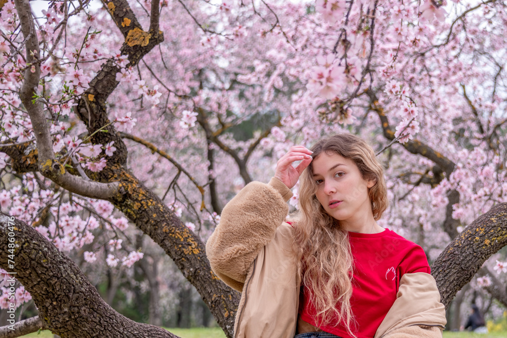 25 year old Caucasian girl with curly blonde hair posing next to blooming almond trees. 25 year old Caucasian girl with curly blonde hair posing next to blooming almond trees.