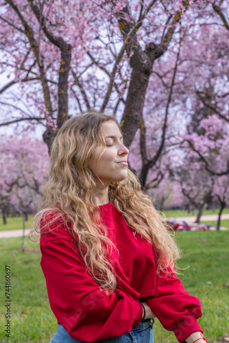 25 year old Caucasian girl with curly blonde hair posing next to blooming almond trees.